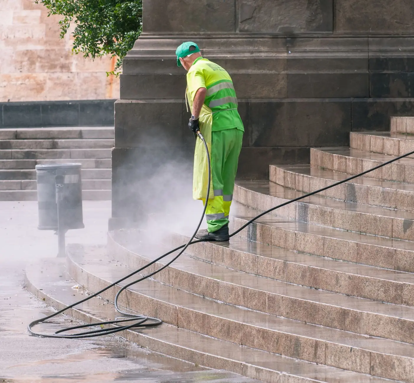 A worker pressure washing stone steps, the cleaned stone visibly brighter