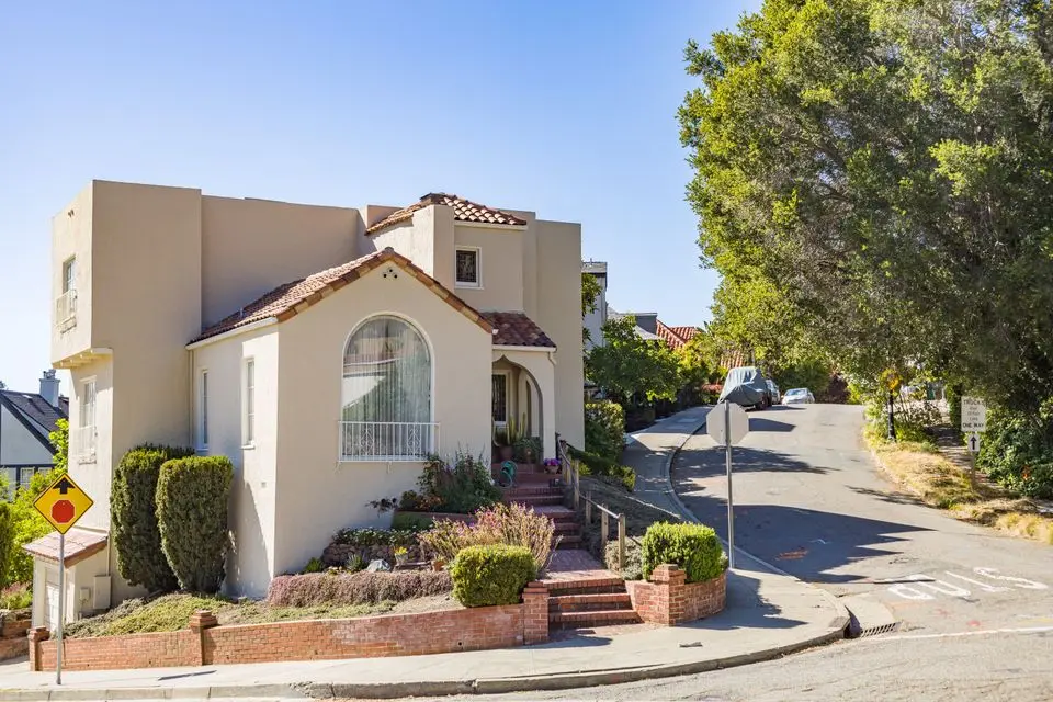 Spanish-style stucco home on a sunny street corner with a landscaped front yard