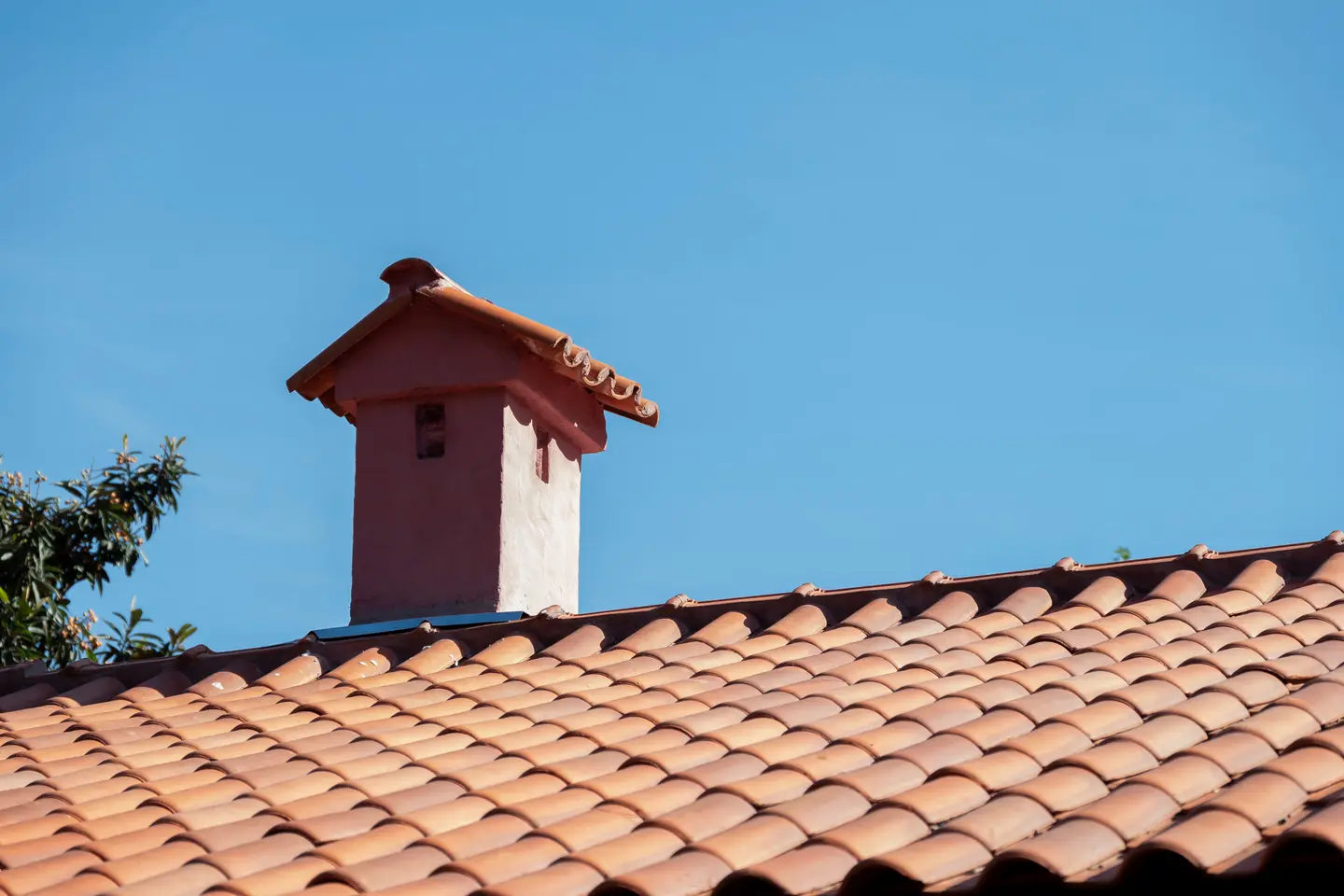 Red clay tile roof with a chimney under a clear blue sky