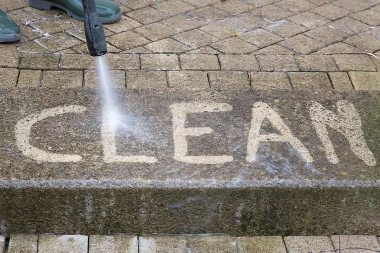 The word CLEAN pressure-washed into grimy pavers, bright stone showing through the dirt