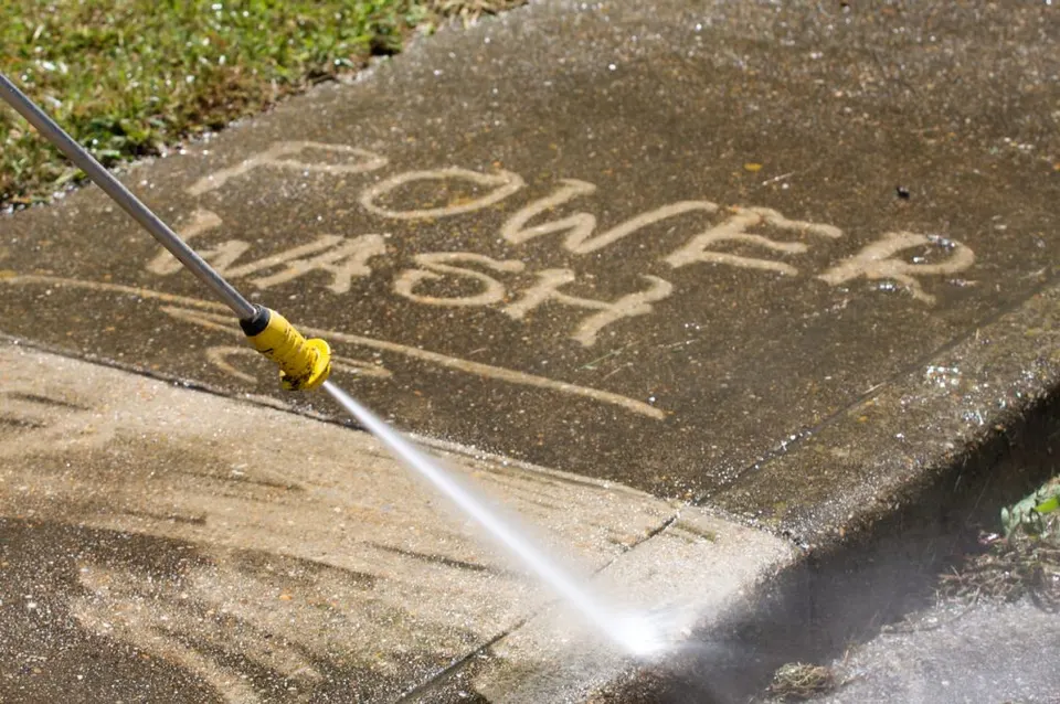 The words POWER WASH cleaned into a dirty sidewalk by a pressure washer