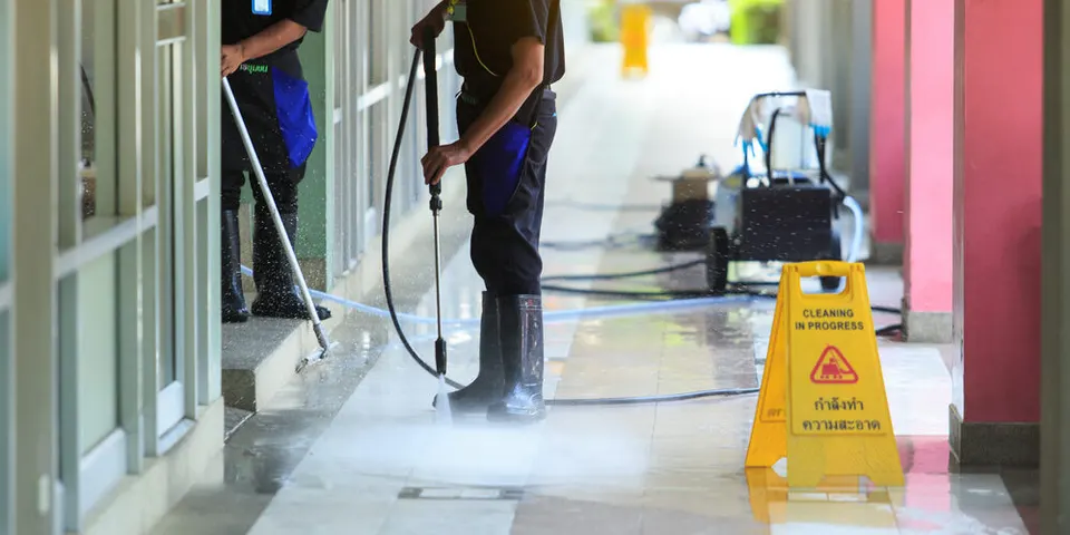 Crew washing a commercial entrance behind a cleaning-in-progress sign